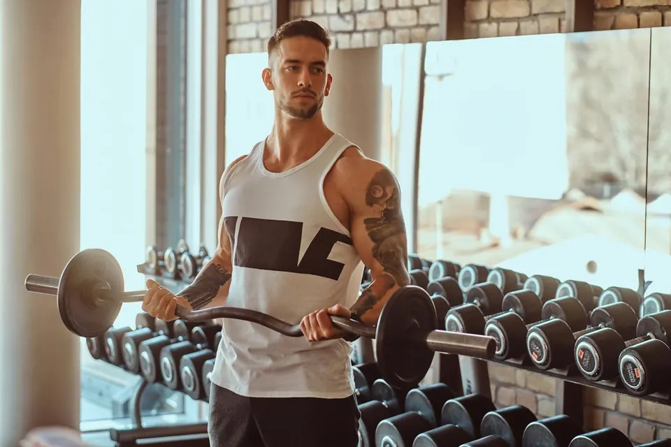 Hombre haciendo curl con barra frente al rack de mancuernas